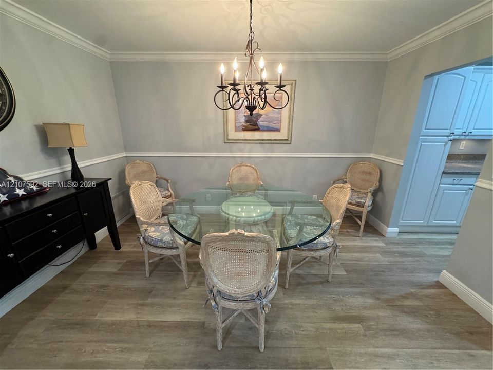 Dining area featuring wood-finish flooring, chair rail molding, crown molding, and a multi-arm candle-style chandelier