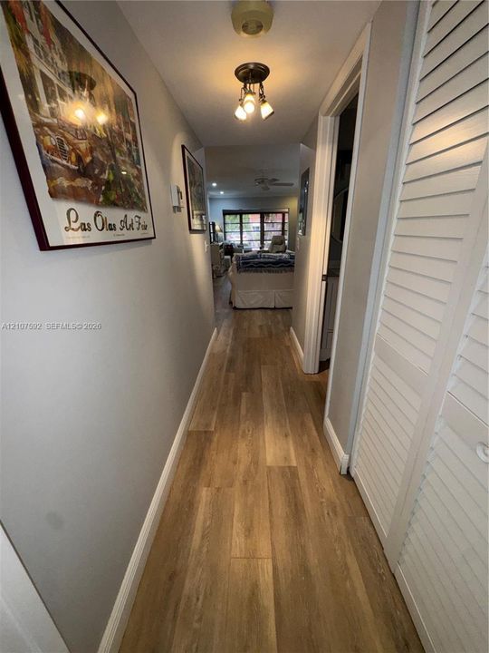 Hallway featuring wood-finish flooring, multi-bulb ceiling lighting, and white louvered closet doors