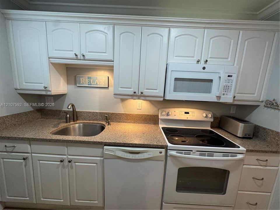 Kitchen featuring white cabinetry, solid surface countertops, stainless steel sink with a high-arch faucet, built-in microwave, and electric range