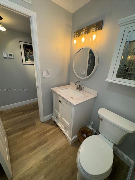 White vanity with a stone countertop, circular wall mirror, wood-finish flooring, three-light fixture, and wall-mounted medicine cabinet