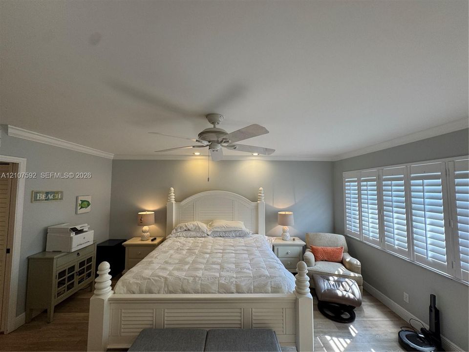 Room featuring wood-finish flooring, plantation shutters, crown molding, and a central ceiling fan