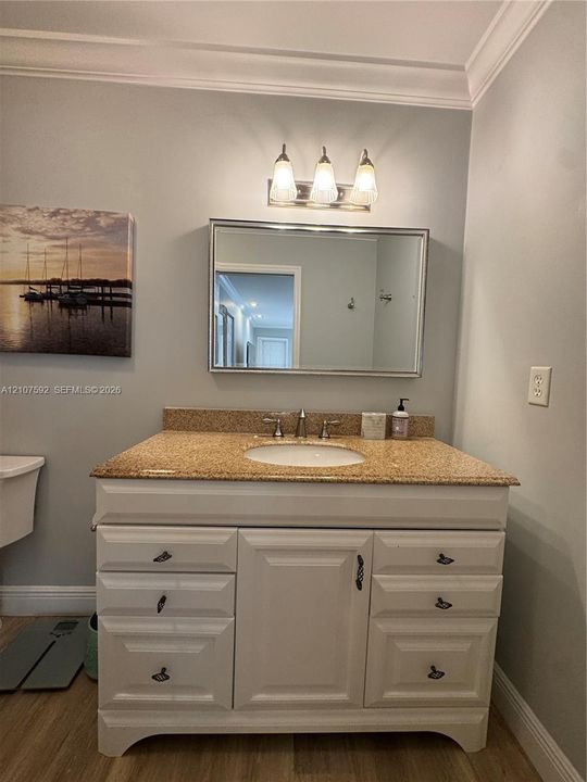 White cabinetry vanity featuring an integrated oval basin, speckled stone-finish countertop, three-light polished chrome fixture, and a framed wall-mounted mirror