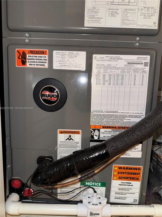 Ruud heating and cooling system featuring metallic grey finish, insulated copper refrigerant lines, and PVC drainage piping