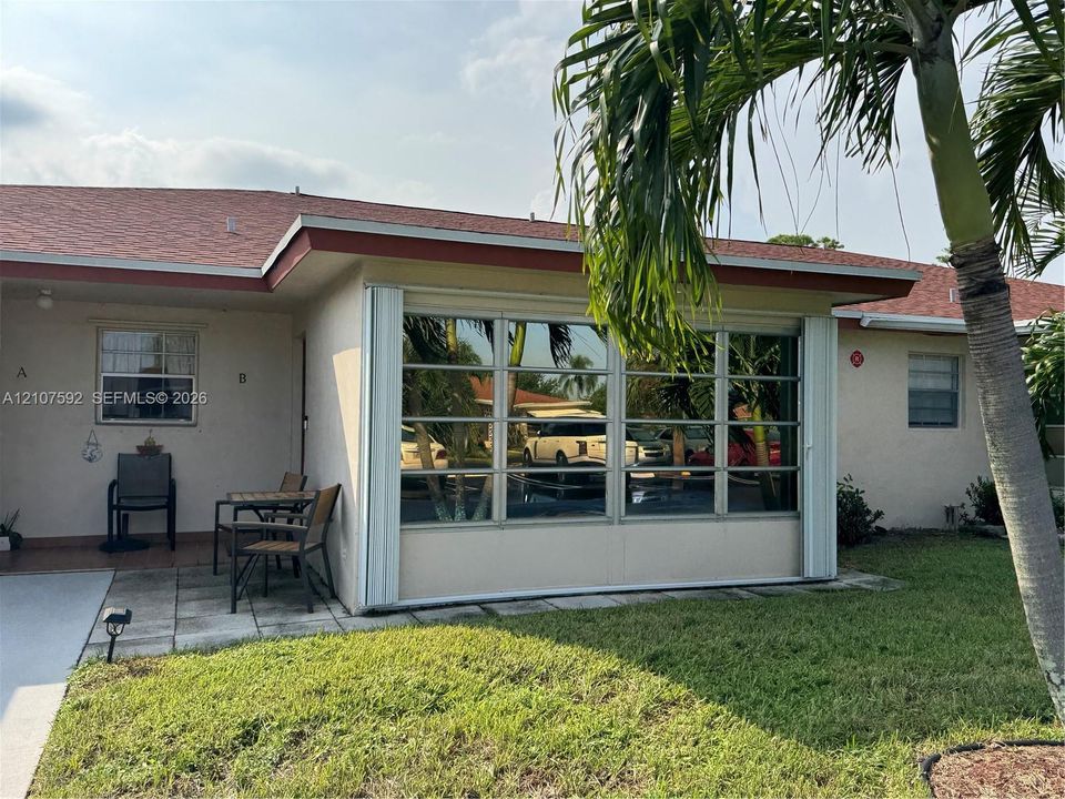 Stucco exterior featuring an enclosed sunroom with multi-pane windows, a concrete paver patio, and mature palm trees