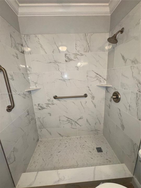 Walk-in shower featuring large-format stone-patterned wall tile, recessed corner shelving, a textured pebble floor, and brushed-finish plumbing fixtures