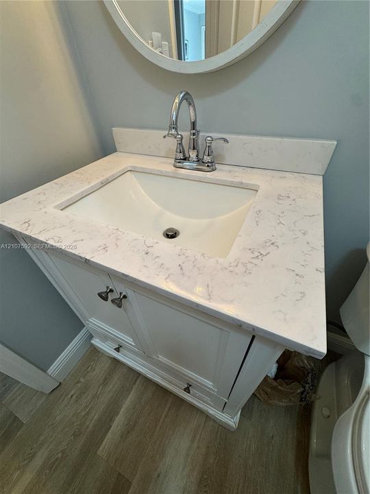 White vanity cabinet with integrated storage, engineered stone countertop, undermount sink, dual-handle chrome faucet, and circular wall-mounted mirror