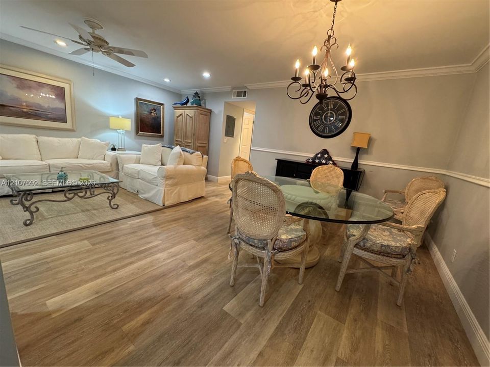 Open-concept living space featuring wood-finish flooring, crown molding, chair rail trim, a multi-arm chandelier, and a ceiling fan