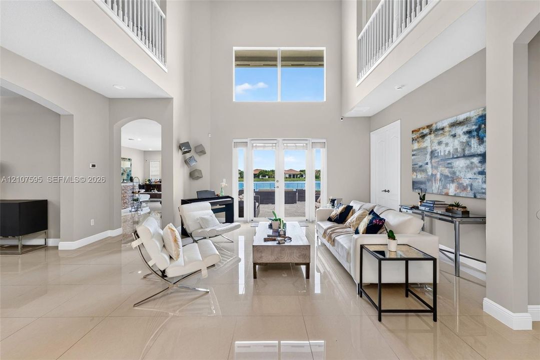 Grand foyer featuring soaring double-height ceilings, large-format tile flooring, a multi-story glass window configuration, arched architectural openings, and glass-paned double doors