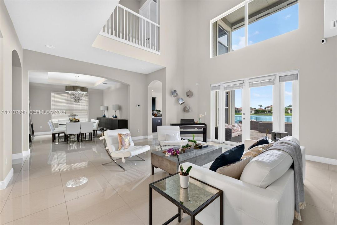 Double-height living area featuring large windows, polished tile flooring, arched doorways, and a mezzanine balcony with a white railing