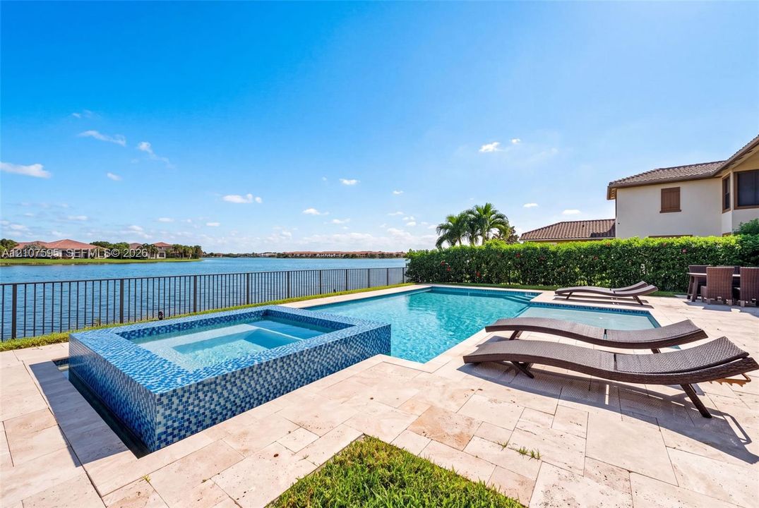 In-ground swimming pool and raised spa featuring blue tile finish, surrounded by a natural stone paver deck and metal perimeter fencing