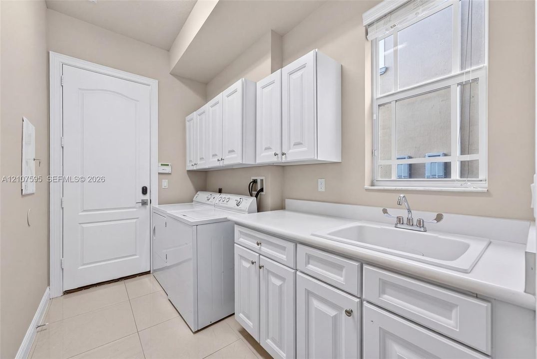 Laundry area featuring white cabinetry, a built-in drop-in sink, solid-surface countertops, and tile flooring