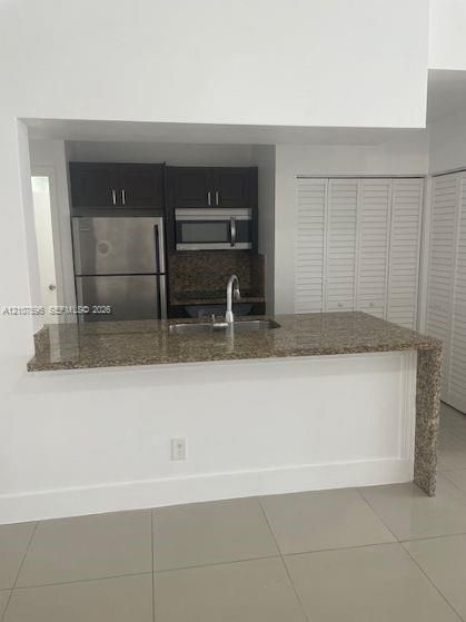 Kitchen featuring stone-finish countertops, stainless steel refrigerator, built-in microwave, dark wood cabinetry, and large-format tile flooring