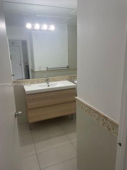Modern vanity with a rectangular sink, light wood-finish cabinetry, ceramic tile flooring, and a decorative mosaic tile backsplash