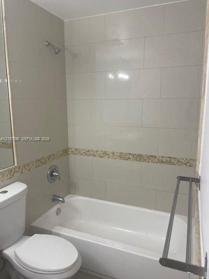 Full-size bathtub with shower combination, large-format neutral wall tile, decorative stone mosaic tile accent border, wall-mounted metal towel rack, and polished chrome fixtures