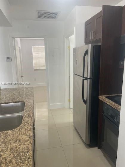 Kitchen featuring stone-finish countertops, stainless steel refrigerator, dark-toned cabinetry, double-basin sink, and tile flooring