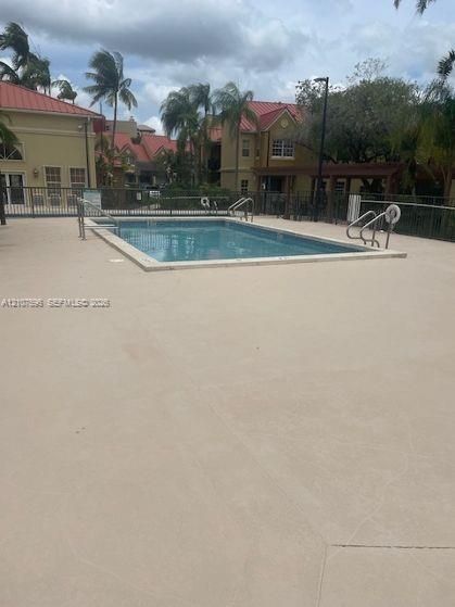 In-ground swimming pool featuring a concrete deck, metal perimeter fencing, and stainless steel ladder rails