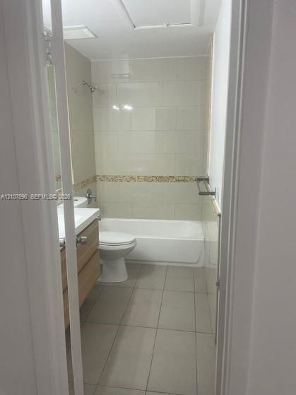 Full bathroom featuring a tub-shower combination with tile surround, wood-finish vanity, large-format floor tile, and wall-mounted hardware