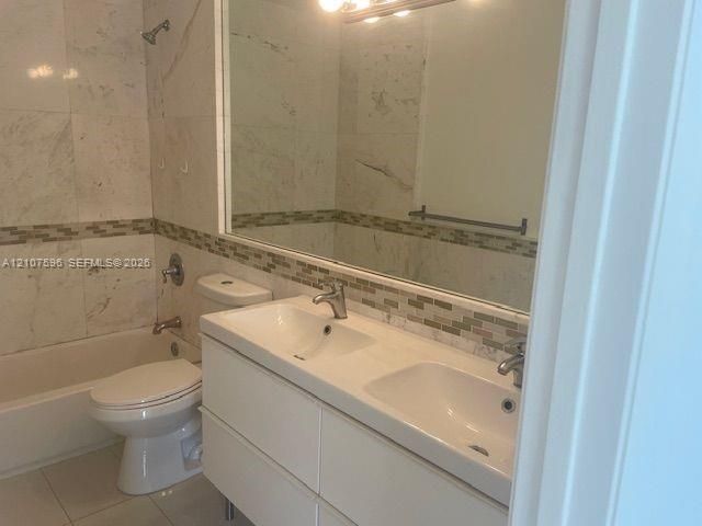 Bathroom featuring a dual-sink vanity with a white countertop, large wall-mounted mirror, mosaic tile backsplash, and a tiled shower-tub combination