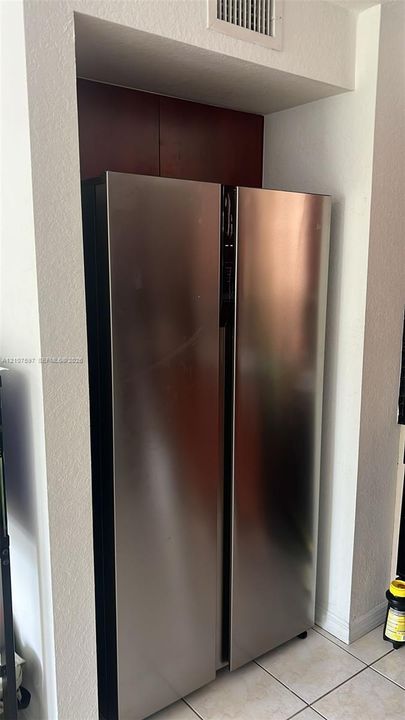Stainless steel side-by-side refrigerator recessed into a custom built-in nook featuring dark wood-finish cabinetry