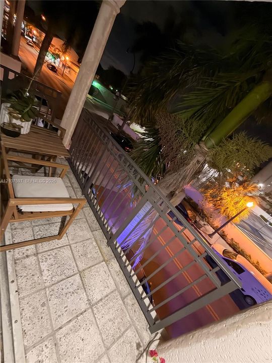 Balcony featuring stone-tile flooring, decorative metal railing, and a columned support structure