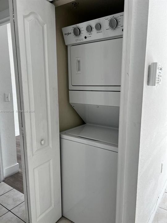 Enclosed laundry closet featuring a stacked white washer and dryer unit