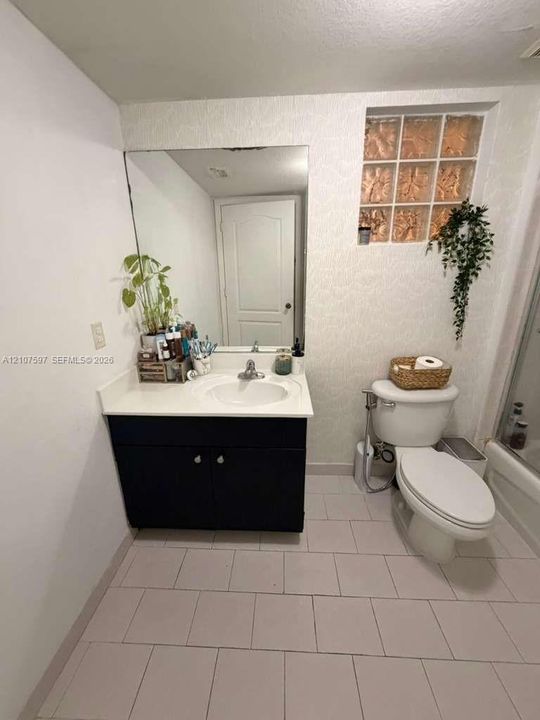 Bathroom featuring a vanity with a white countertop and integrated sink, a large wall-mounted mirror, glass block window accent, and neutral tile flooring