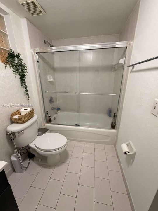 Bathroom featuring a shower and bathtub combination with a glass sliding door, ceramic tile flooring, and wall-mounted metal towel rack