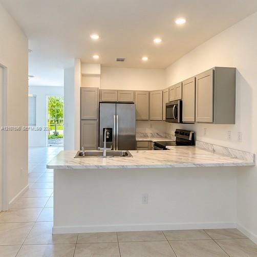 Kitchen featuring light-toned cabinetry, stone-patterned countertops, stainless steel appliances, recessed ceiling lighting, and ceramic tile flooring