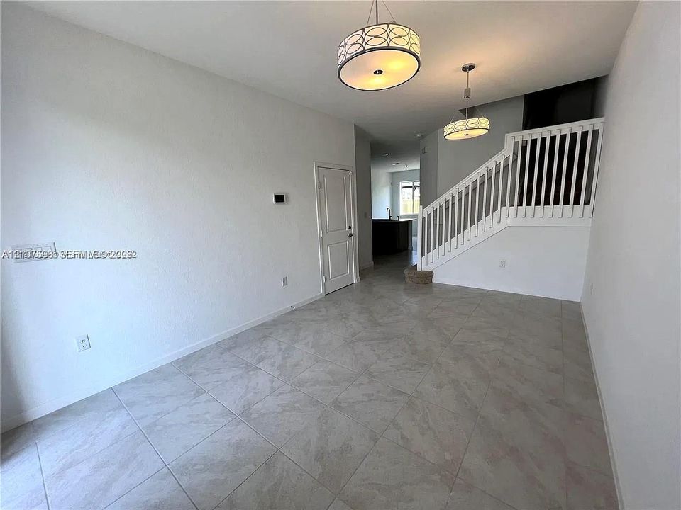 Large-format tile flooring, dual drum pendant lighting, and a staircase featuring a white wooden balustrade