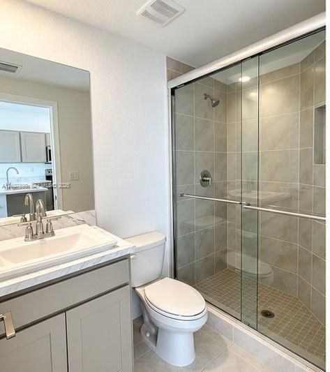 Bathroom featuring a vanity with light-toned cabinetry, solid surface countertop with integrated basin, shower with sliding glass doors and ceramic wall tile, and built-in shower niche