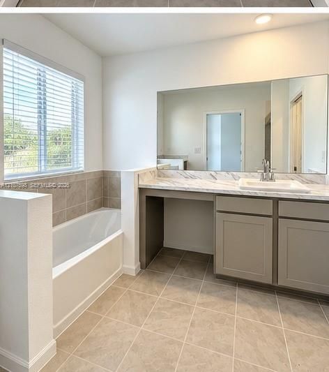 Bathroom featuring a soaking tub with tile surround, vanity with stone-patterned countertop, under-mount sink, large wall-mounted mirror, and tile flooring