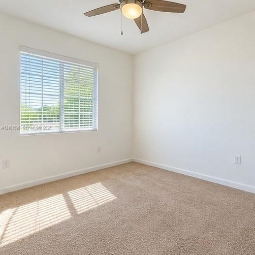 Neutral-toned wall-to-wall carpeting, window with horizontal blinds, and a multi-blade ceiling fan with a central light fixture