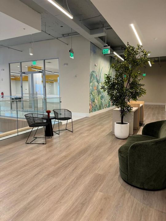 Open-concept interior featuring wood-finish flooring, exposed industrial-style ceiling, glass partition with metal frame, and full-wall decorative mural
