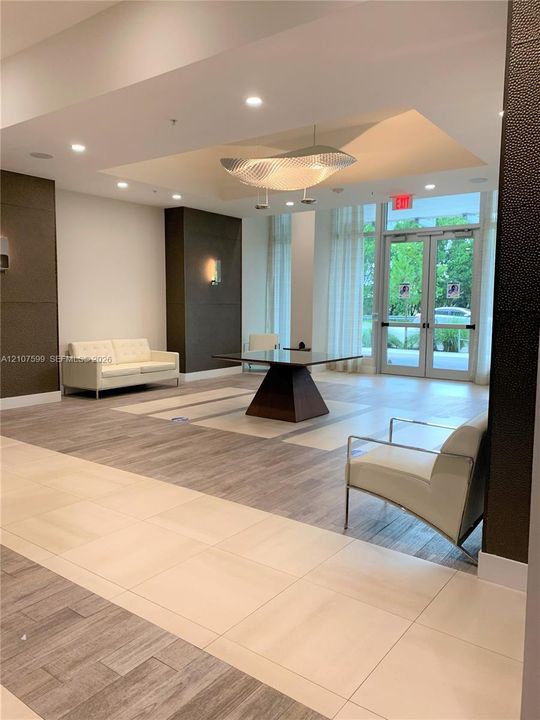Lobby featuring dual-tone tile and wood-finish flooring, a recessed ceiling with a central pendant light fixture, and floor-to-ceiling glass-paneled entry doors
