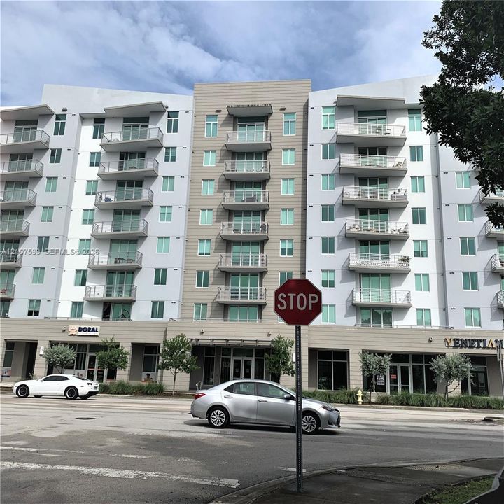 Multi-story building exterior featuring a mixed-material facade, private glass-railed balconies, and ground-level commercial storefronts