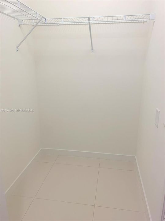 Walk-in storage space featuring large-format neutral floor tile and white coated-wire shelving