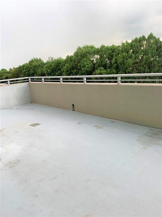 Outdoor terrace featuring a solid parapet wall, metal railing, and surface-level drainage