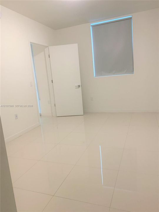 Interior space featuring high-gloss tile flooring, smooth neutral walls, and a single-panel interior door with brushed metal hardware