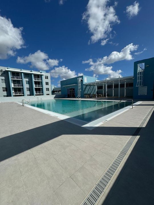 Swimming pool with tile surround, metal pool ladders, pergola-covered deck area, and multi-story building exterior