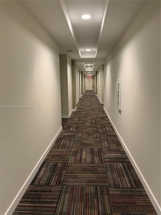 Hallway featuring recessed ceiling lighting, a dropped ceiling architectural detail, and patterned carpet flooring