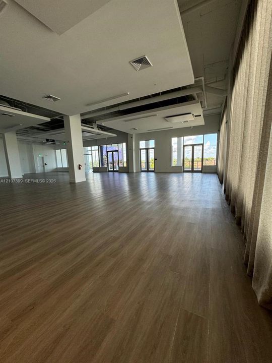 Open-concept interior featuring wood-finish flooring, recessed ceiling architectural elements, multiple glass-paneled entryways, and floor-to-ceiling windows