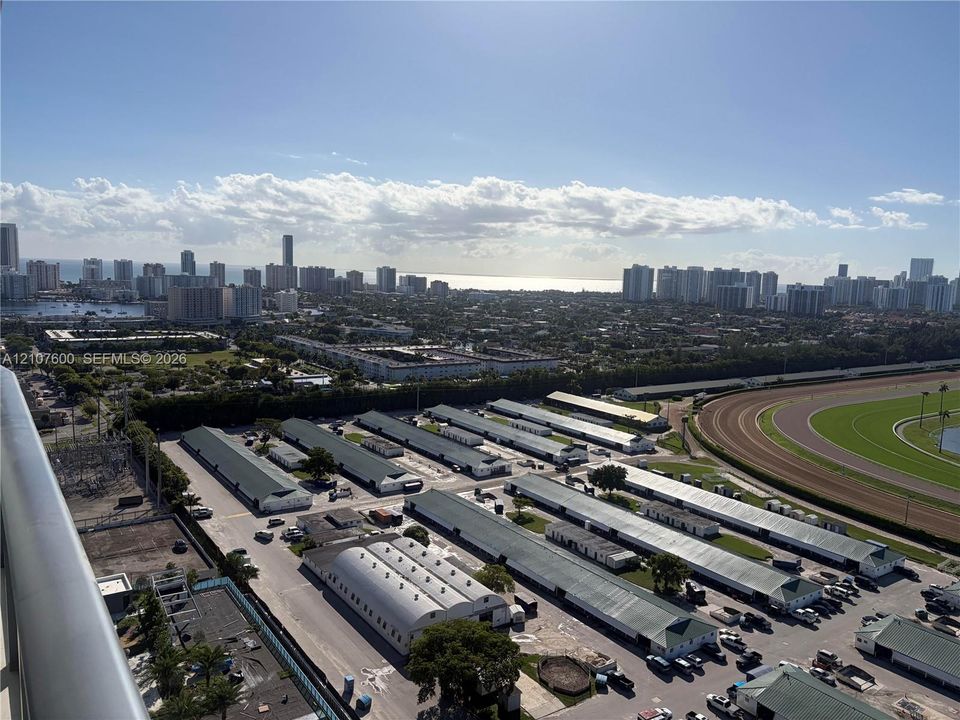 Elevated perspective featuring coastal city skyline, ocean horizon, and racetrack grounds