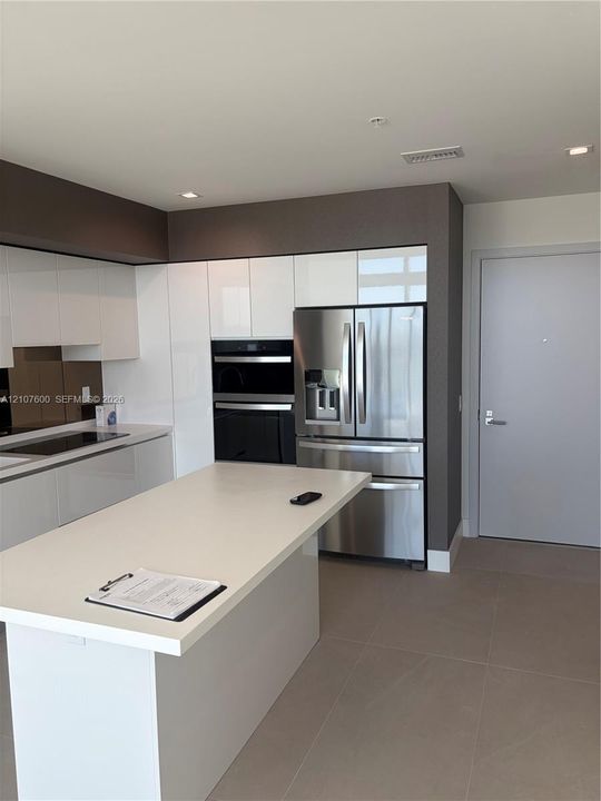 Kitchen featuring a central island with a solid surface countertop, high-gloss white cabinetry, stainless steel appliances including a built-in wall oven, and ceramic tile flooring