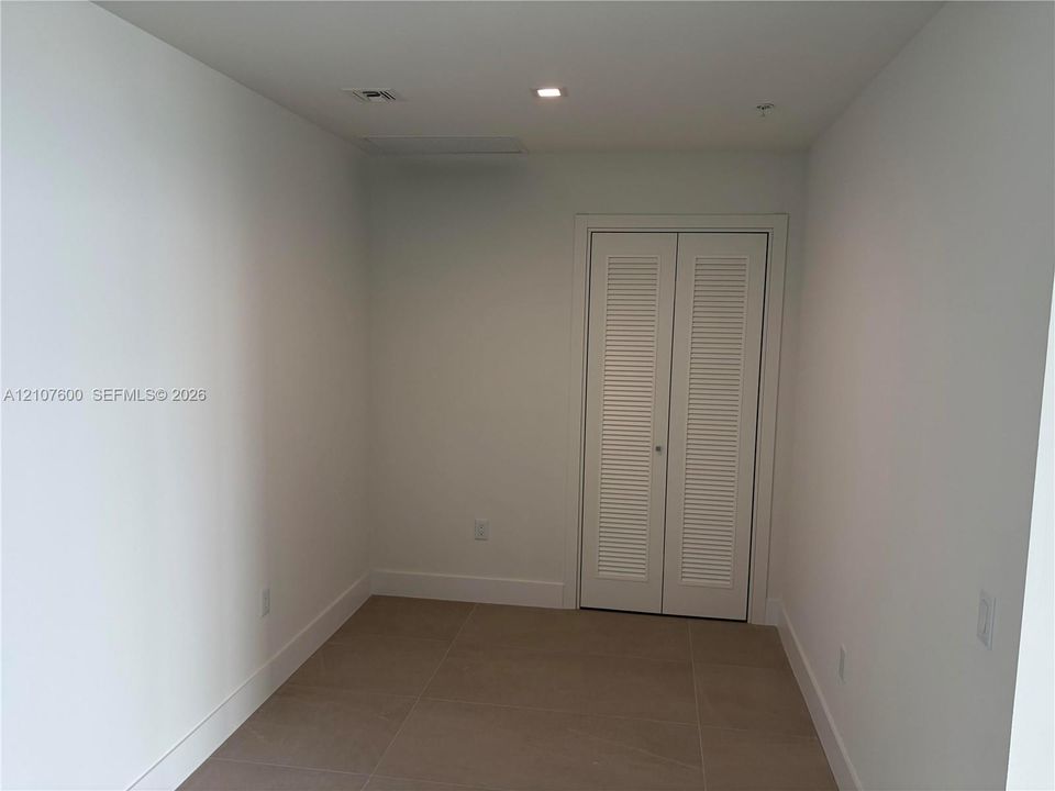 Neutral-toned oversized tile flooring and a double-door closet featuring white louvered panels and recessed lighting- Could be use as a 3rd Bed, Family or dinning room.