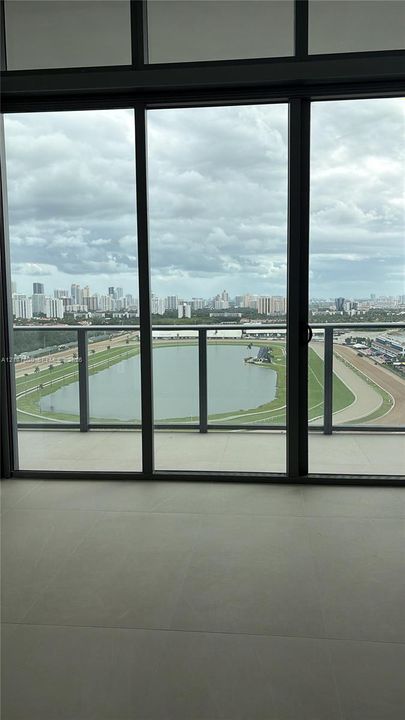 Floor-to-ceiling glass panel windows, sliding glass door, neutral large-format tile flooring, and private balcony featuring a glass railing