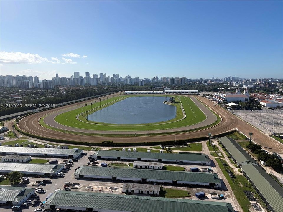 Aerial perspective of a large-scale track facility featuring a central grassed oval, an expansive interior water feature, a multi-lane dirt track, and rows of metal-roofed structures
