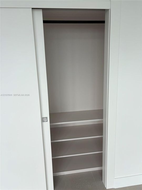 Storage space featuring a white sliding door, square chrome-finish hardware, three built-in shelves, and a horizontal hanging rod