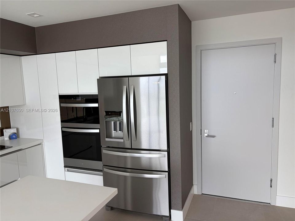 Kitchen featuring flat-panel white cabinetry, integrated stainless steel double wall ovens, a stainless steel French-door refrigerator, and solid-surface countertops