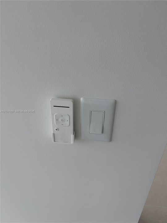 Wall-mounted white remote control cradle and standard rocker light switch in living room and both beedrooms