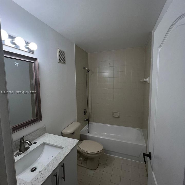 Bathroom featuring a stone-composite countertop with an integrated basin, three-light vanity fixture, framed wall mirror, and a tub-shower combination with ceramic tile surround